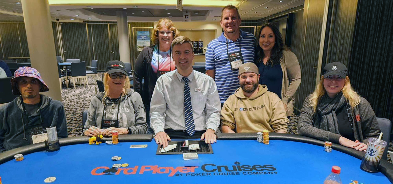 2024 March Main Event - seven peaple standing on either side of a dealer seated at a blue poker table. 